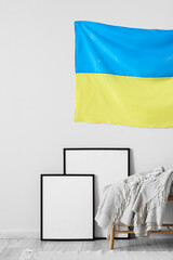 Wall Mural - Bench with plaid, blank photo frames and flag of Ukraine hanging on white wall