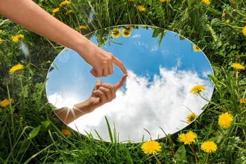 nature concept - hand touching sky reflection in round mirror on summer field