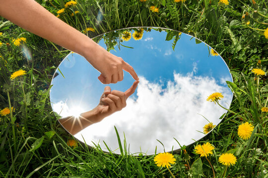 nature concept - hand touching sky reflection in round mirror on summer field