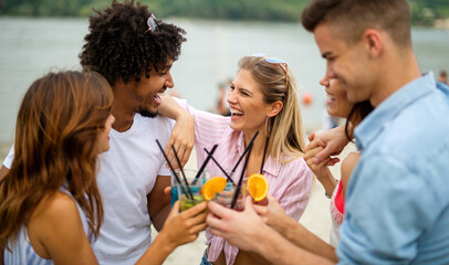 Happy young people, friends having fun on the beach and drinking cocktails together.