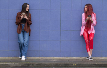 Wall Mural - young female friends with mobile phone on blue wall