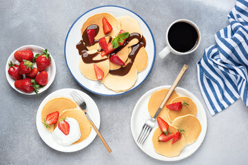 Wall Mural - Pancakes served with fresh strawberries, chocolate syrup and yogurt, concrete table background. Top view. Family breakfast concept