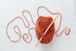 Crochet hook and ball of cotton yarn ocher color on a white table