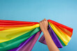 © Pituk - Man's hand holding colorful rainbow flag on blue color background. LGBT concept.