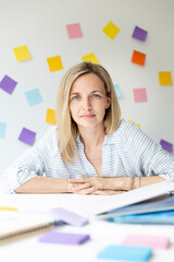 Wall Mural - Portrait of pretty young blonde woman with beautiful laugh sitting at office table in front of white wall with colorful sticky notes