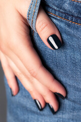 Wall Mural - Female hand with beautiful manicure - dark black nails on jeans denim textile, closeup fingers. Selective focus