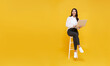 canvas print picture - Young woman asian happy smiling. While her using laptop sitting on white chair and looking isolate on copy space yellow background.