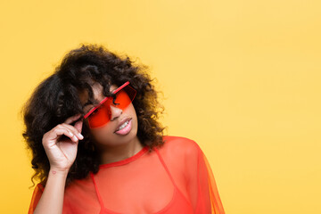 Wall Mural - brunette african american woman adjusting sunglasses and looking away isolated on yellow.