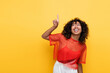 © LIGHTFIELD STUDIOS - smiling african american woman in summer clothes looking up and pointing with finger isolated on yellow.