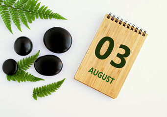 August 03. 03th day of the month, calendar date. Notepad, black SPA stones, green leaves. Summer month, day of the year concep