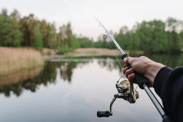 Wall Mural - Fisherman with rod, spinning reel on the river bank. Man catching fish, pulling rod while fishing from lake or pond with text space. Fishing for pike, perch on beach lake or pond. Fishing day concept.