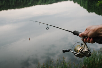 Wall Mural - Fisherman with fishing rod, spinning reel on the background river bank. Sunrise. Fishing the backdrop of lake.