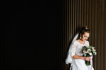 Wall Mural - Young beautiful bride in elegant dress is standing and holding hand bouquet of white flowers and greens with ribbon.