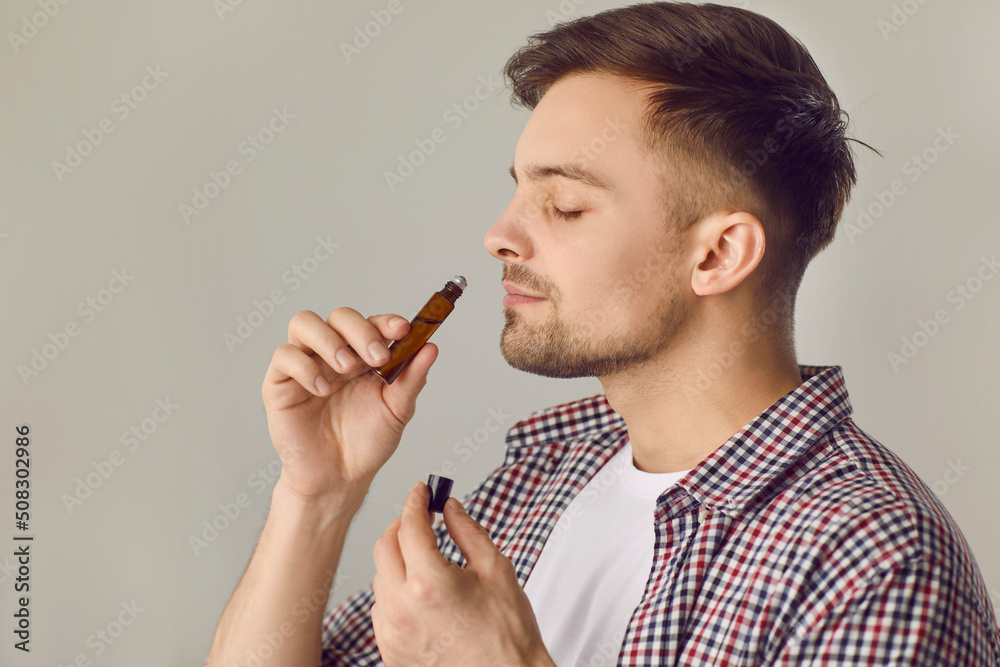 Happy young man smelling good quality essential oil. Side view portrait of  handsome man holding roller bottle to his nose and enjoying wonderful scent  of natural essential oil. Aromatherapy concept Stock Photo |