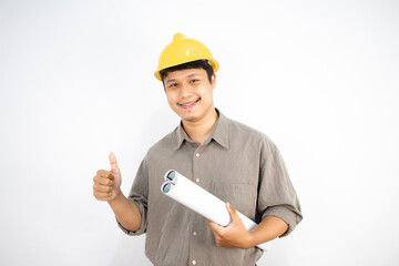 Asian male engineer wearing a helmet and holding a blueprint looks at the camera and smiles with determination on a white background.