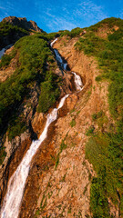 Wall Mural - a small waterfall flows down the slope of a rock against a beautiful blue sky