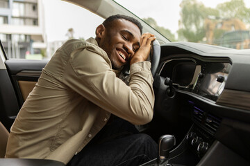 Wall Mural - Delighted African American man hugging the steering wheel of his new car, closing his eyes and smiling