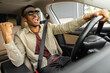 © Home-stock - A joyful African American in glasses dances in a car, sings while driving his car. Road fun