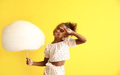 Wall Mural - Little African-American girl with cotton candy on yellow background