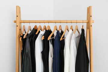 wooden rack with female clothes near light wall