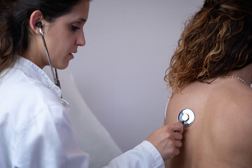 Doctor visits patient in her office. Doctor listens to the patient's chest with a stethoscope, observing the breathing and internal noises of the organism. Traditional medical examination.