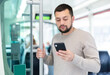 © JackF - Interested young man browsing messages on phone on way to work in modern streetcar ..
