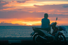 Woman Sitting On The Scooter By The Sea And Enjoying The Colorful Sunset