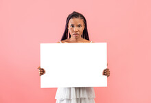 Serious Young Black Woman Holding Empty Paper Banner With Mockup For Design On Pink Background