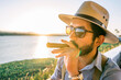 Latin young man wearing glasses, hat and suspenders smoking a cigar in a bar on the shore of a lake at sunset in Managua Nicaragua