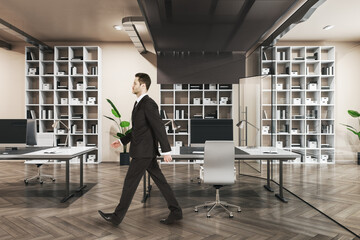 Poster - Attractive thoughtful european businessperson walking in wooden and concrete office interior with furnituire and window with city view. CEO, executive and consulting concept.