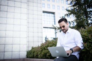 Wall Mural - Casual dressed business man working on laptop outdoors