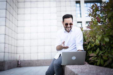 Wall Mural - Young and casual dressed business man outdoors, having a conference call on laptop