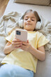 © Julija - Little girl with mobile phone listening to music while lying on sofa.
