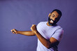 portrait of a successful man dancing with a beard and a blue t-shirt celebrating with arm up on a purple background studio
