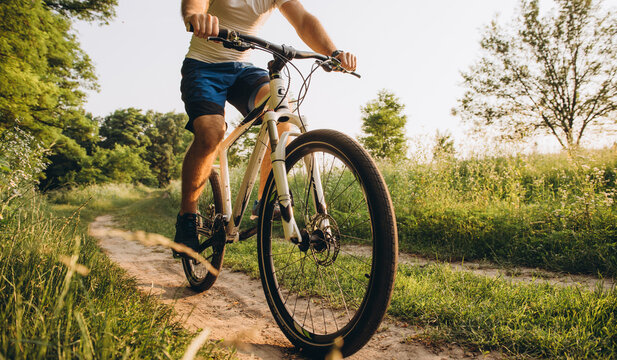 A man rides a bicycle on a dirt road in the summer at sunset. Active rest in the summer on bicycles.