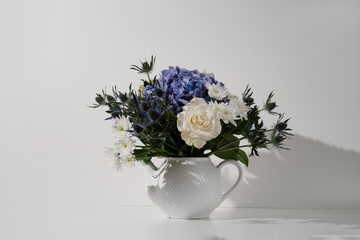 Flower bouquet with rose hydrangea chrysanthemum eryngium in a teapot on white background in sunlight. Modern hipster composition cottagecore sideview