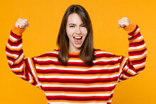 Young Happy Excited Caucasian Woman In Red Striped Sweatshirt Showing Biceps Muscles On Hand Demonstrating Strength Power Isolated On Plain Yellow Background Studio Portrait. People Lifestyle Concept.