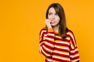 Wall Mural - Young sad mistaken caucasian woman 20s in red striped sweatshirt look aside on workspace area mock up biting nails fingers isolated on plain yellow background studio portrait People lifestyle concept