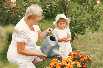 Wall Mural - Little girl and her grandmother watering flowers in garden