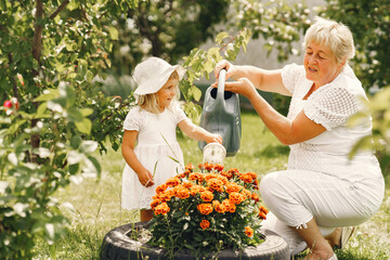 Wall Mural - Little girl and her grandmother watering flowers in garden