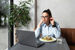 © Srdjan - Young freelancer business woman watching movie on her laptop computer during her lunch break. Exchange student waiting for video call with her family while she eating big portion of chicken dish