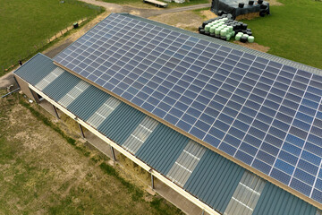 Aerial view of blue photovoltaic solar panels mounted on farm building roof for producing clean ecological electricity. Production of renewable energy concept