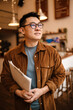 © Drobot Dean - Adult asian man smiling and holding paper documents in cafe indoors