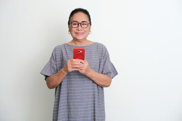 Wall Mural - Elderly Asian woman smiling to the camera while holding a mobile phone