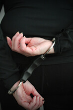 A Woman Being Arrested And Standing With Her Hands In Handcuffs Behind Her Back. The Arrested Prisoner Is Facing The Wall.