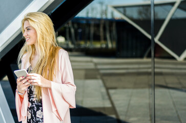 Wall Mural - happy blonde young woman outdoor using her mobile phone