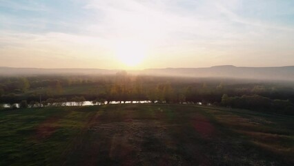 Wall Mural - Aerial view of a misty river surrounded with green trees at foggy sunrise. Calm morning and relaxing atmosphere. Beautiful landscape