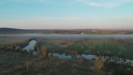 Wall Mural - Aerial view of a misty river surrounded with green trees at foggy sunrise. Calm morning and relaxing atmosphere. Beautiful landscape