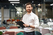 Front view of brunette male with beard standing, holding folder in furniture store. Designer, seller, architect writing, designing, looking at camera. Concept of furniture.