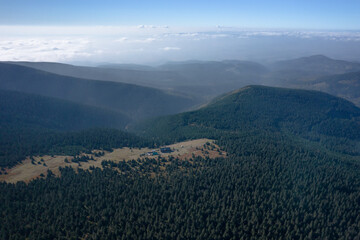  Aerial landscape of the green mountains. Clouds low over the peaks in the background, clear blue sky.